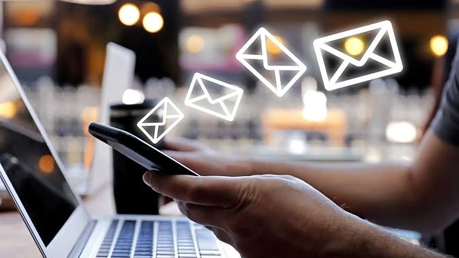 Emails flying out of a phone held over a laptop, on their way to the inbox