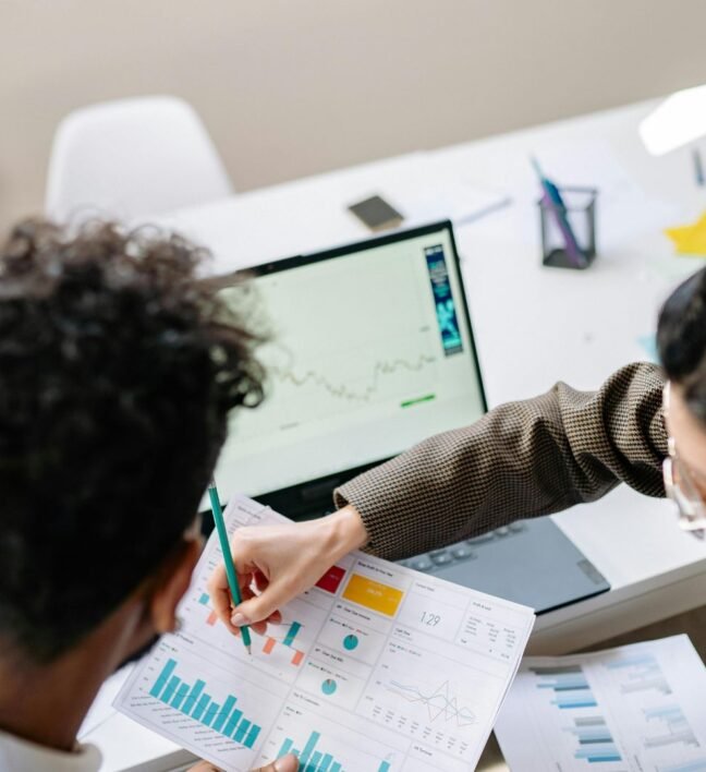 Two marketers analyzing charts and website data on a computer screen, representing SEO strategy, topic clusters, and content planning.